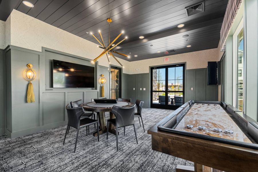 Modern game room with card table, black chairs, TV, unique chandelier, and shuffleboard table.
