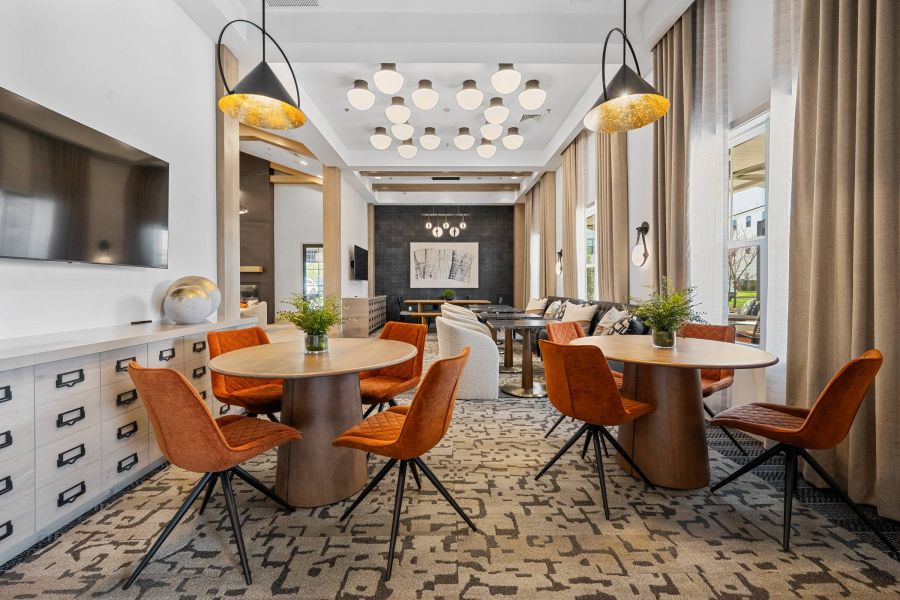 Modern lounge with orange chairs, round tables, pendant lights, TV, and large windows with beige curtains.