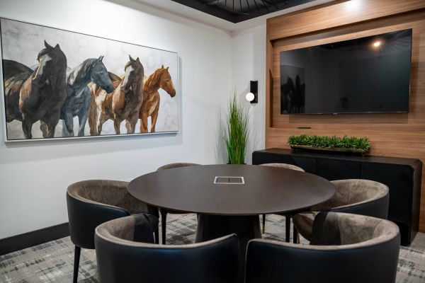 Modern meeting room with round table, five chairs, horse painting, and wall-mounted TV.