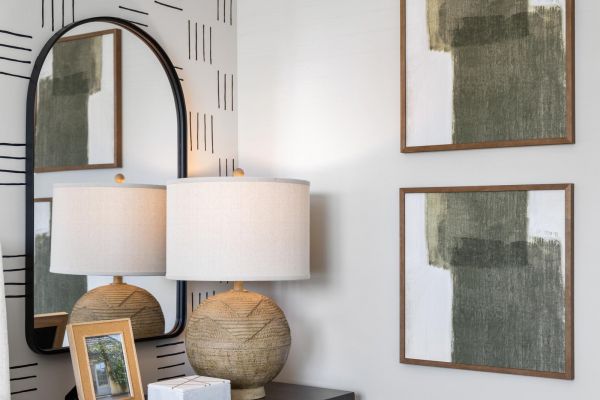 Modern bedroom corner with a black dresser, lamp, mirror, framed art, and abstract wall decor.