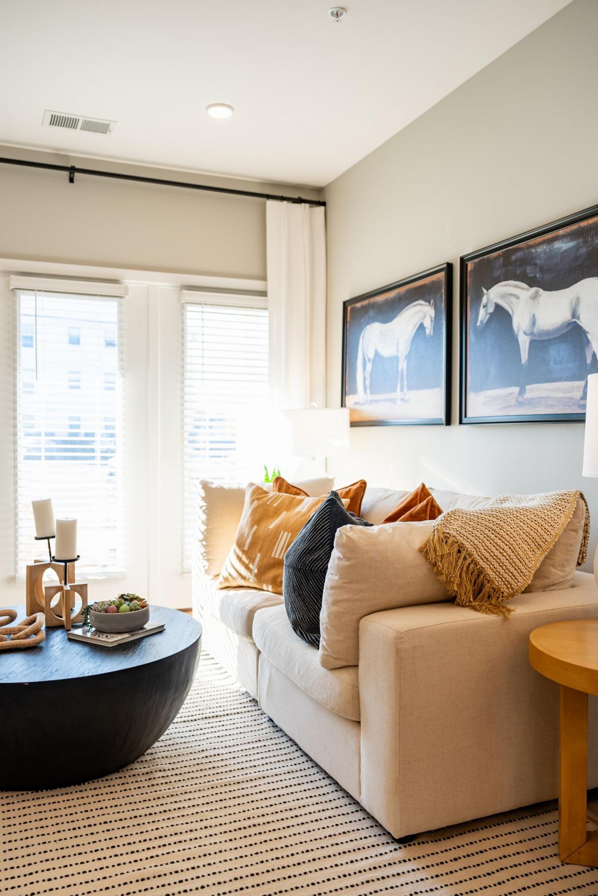 Bright living room with a beige sofa, throw pillows, round coffee table, and horse artwork on the wall.