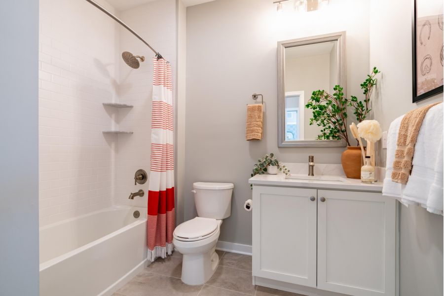 Modern bathroom with white vanity, toilet, tub, red-striped shower curtain, and decorative plants.