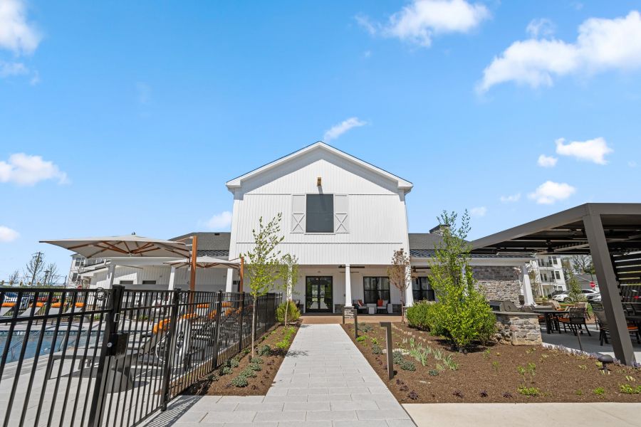 Modern white building with poolside seating, a fenced pool, and landscaping under a bright blue sky.