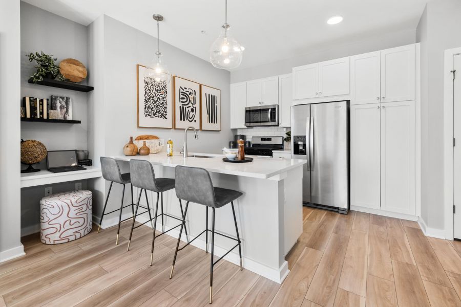 Modern kitchen with white cabinets, island seating, stainless steel appliances, and decorative shelves.