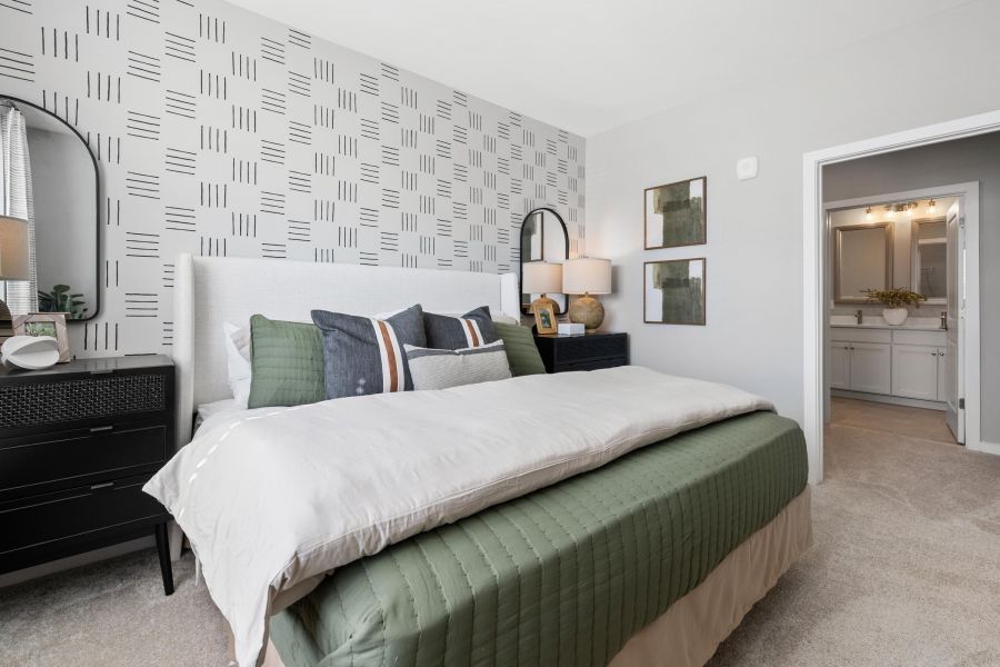 Modern bedroom with geometric accent wall, green bedding, black nightstands, and view into a bathroom.