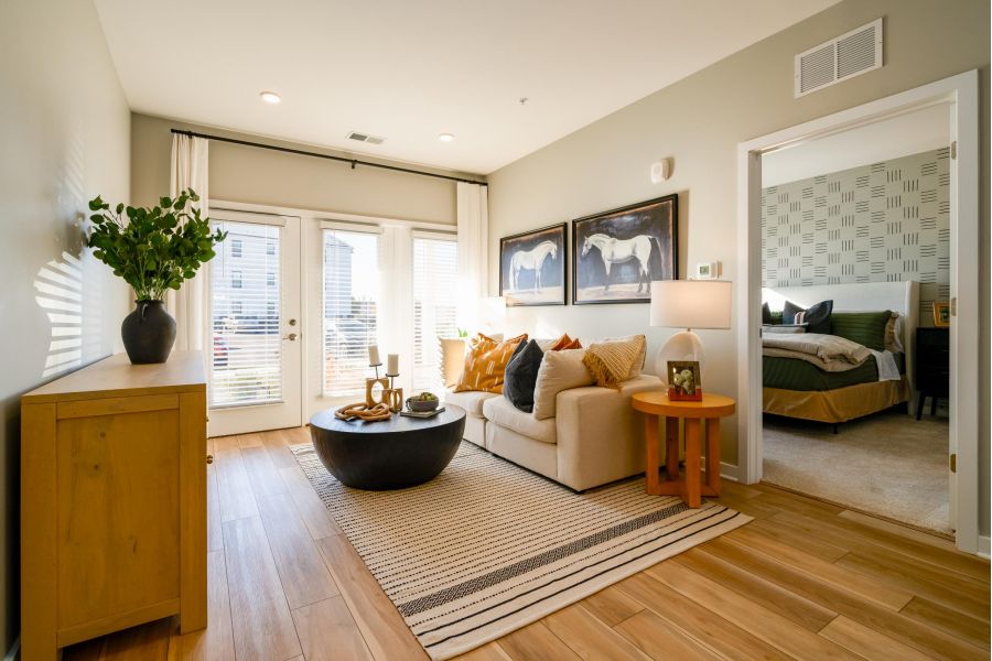 Bright living room with a beige sofa, coffee table, and open doorway leading to a bedroom.