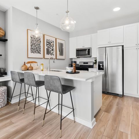 Modern kitchen with white cabinets, island seating, stainless steel appliances, and decorative shelves.