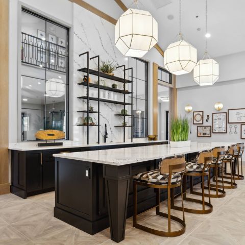 Modern kitchen with black island, marble countertops, bar stools, open shelving, and large pendant lights.